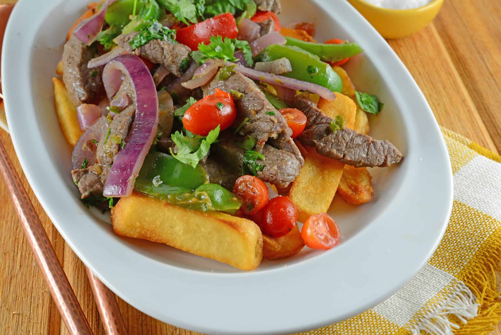 Lomo Saltado is a Peruvian dish using tender steak, onions, tomatoes, bell peppers and jalapenos over crispy French fries.