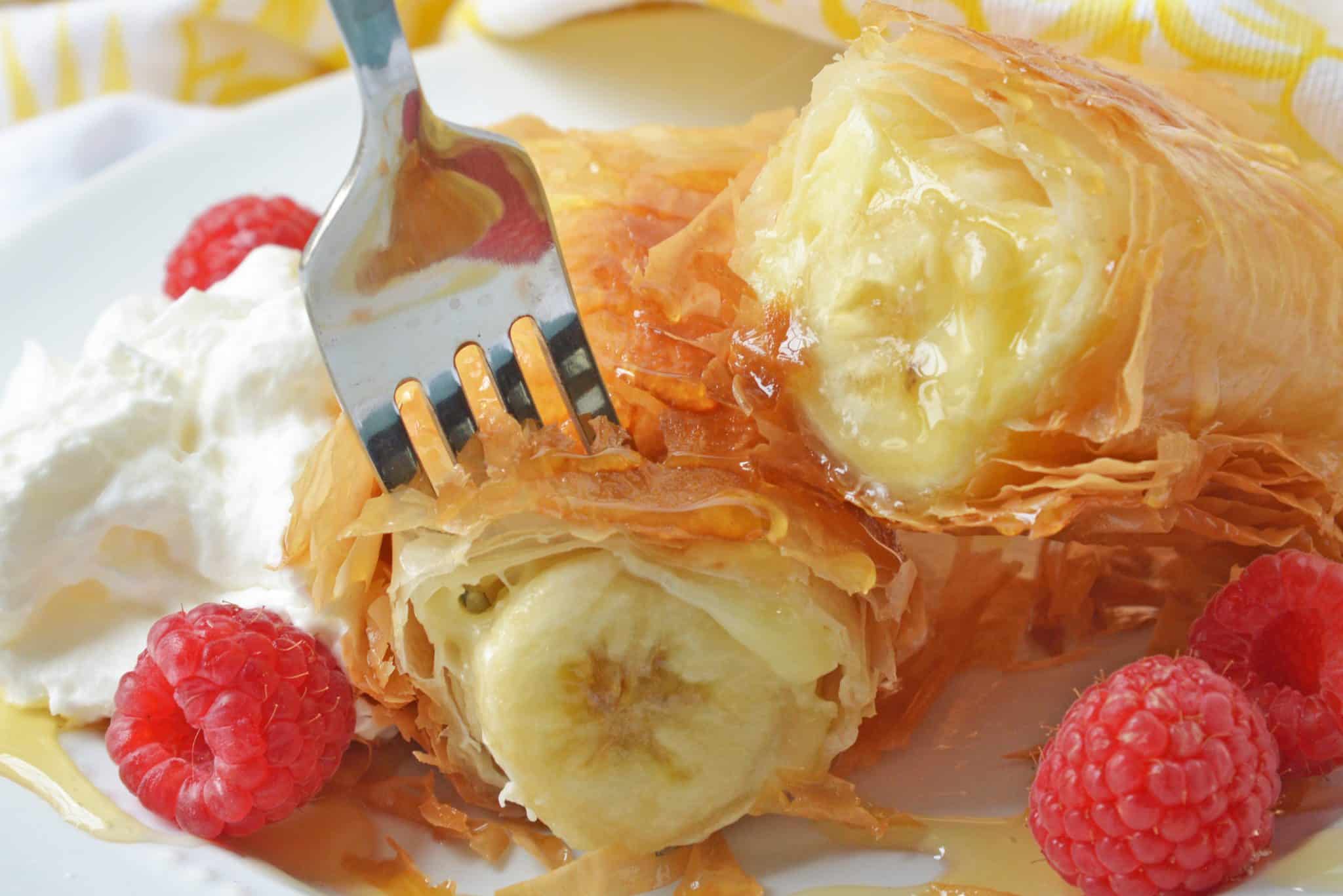 This Banana Fried Cheesecake recipe will become one of your all time favorite desserts! They are fried golden brown to perfection and drizzled with honey. #friedcheesecake #bananaspringrolls www.savoryexperiments.com