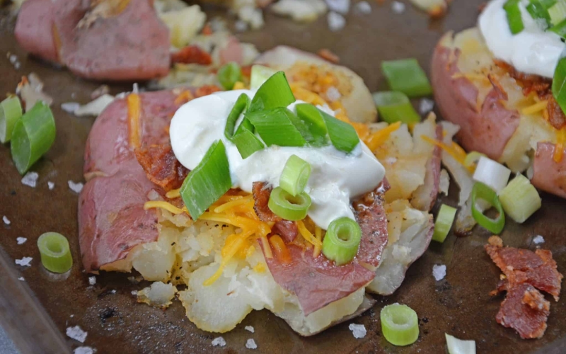 Loaded Smashed Potatoes are a cross between a loaded baked potato and loaded mashed potatoes. Topped with a zesty butter sauce, cheese, bacon, sour cream and scallions. #smashedpotatoes #potatorecipes www.savoryexperiments.com