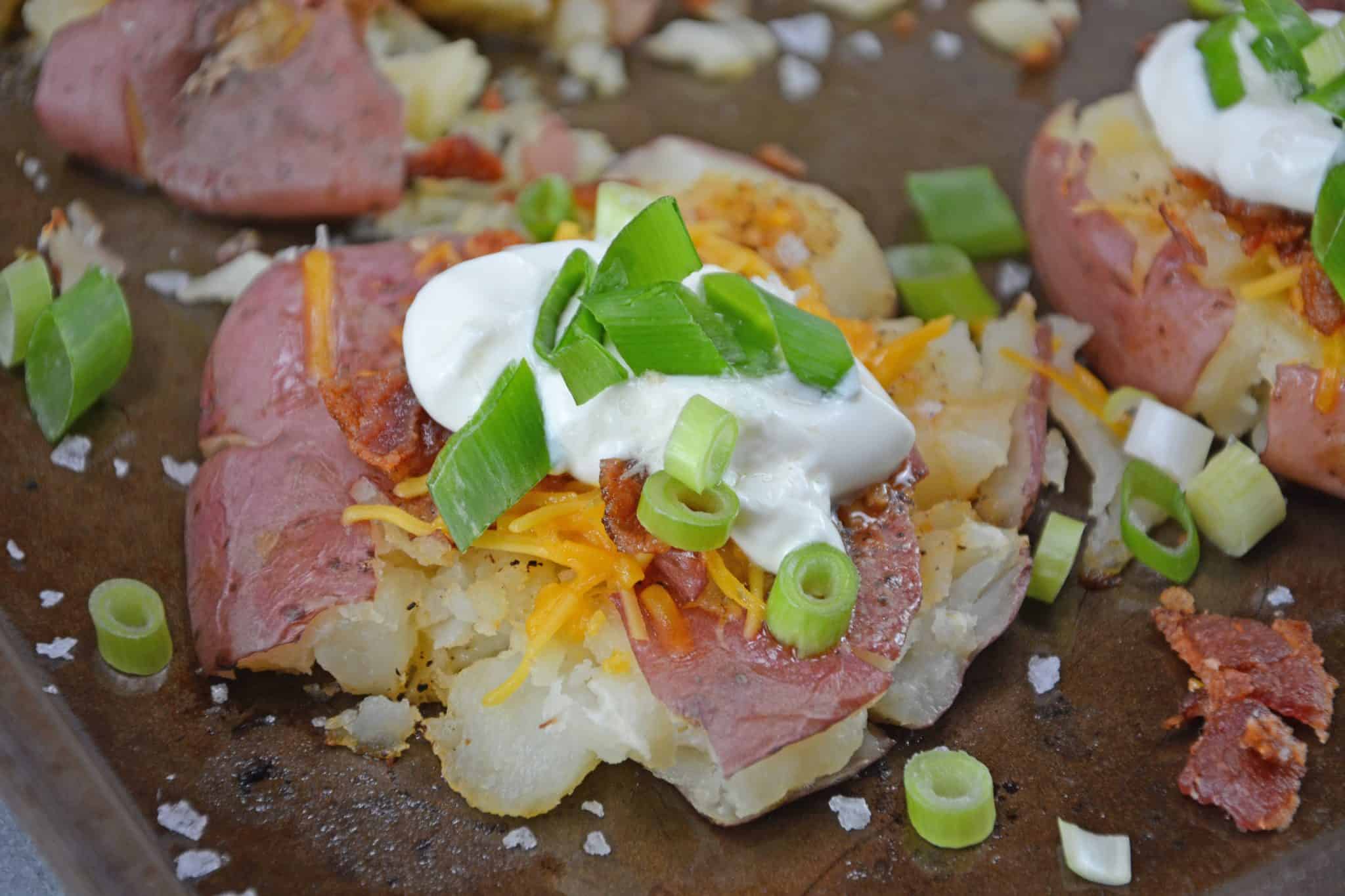 Loaded Smashed Potatoes are a cross between a loaded baked potato and loaded mashed potatoes. Topped with a zesty butter sauce, cheese, bacon, sour cream and scallions. #smashedpotatoes #potatorecipes www.savoryexperiments.com