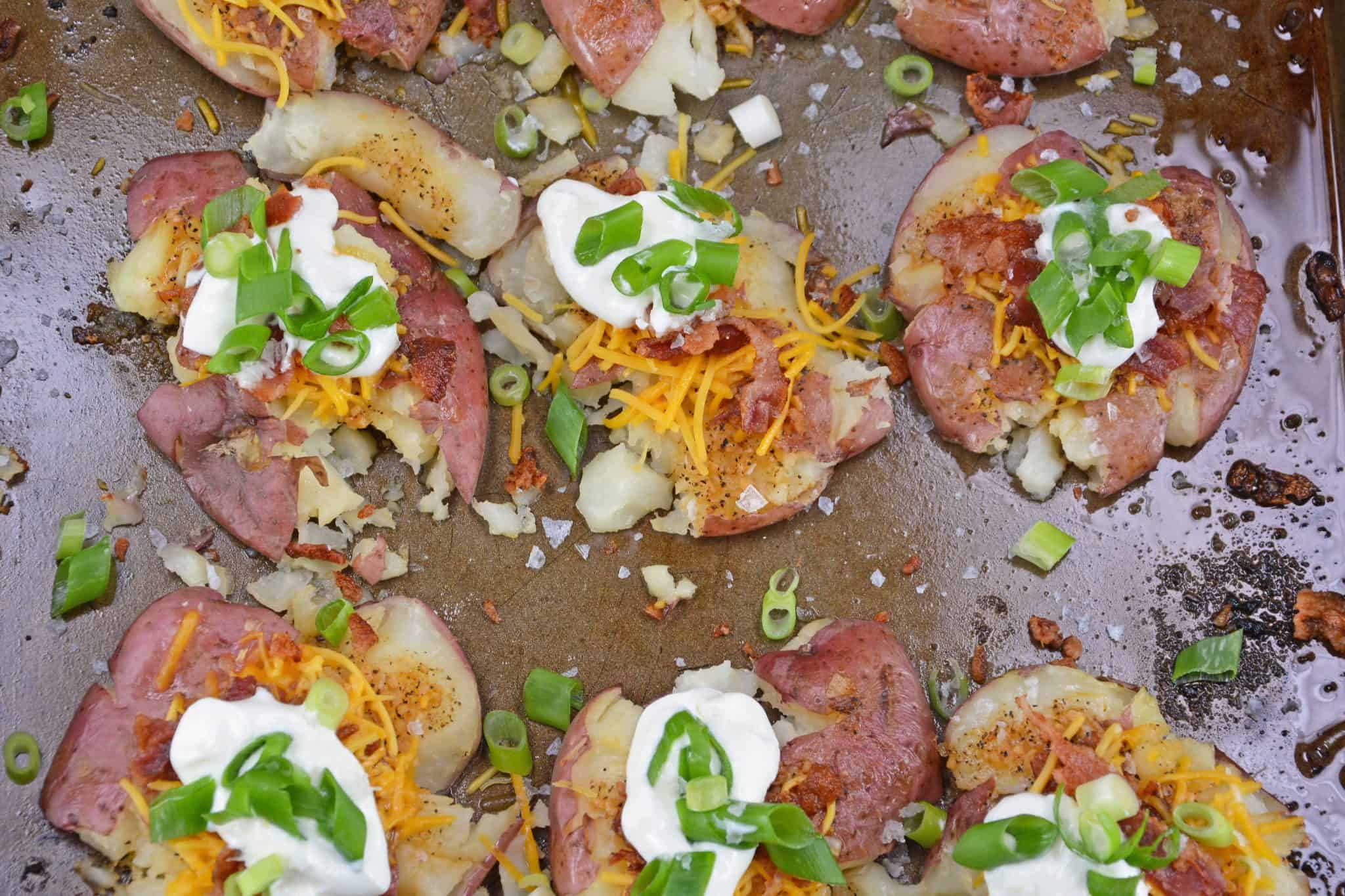 Loaded Smashed Potatoes are a cross between a loaded baked potato and loaded mashed potatoes. Topped with a zesty butter sauce, cheese, bacon, sour cream and scallions. #smashedpotatoes #potatorecipes www.savoryexperiments.com