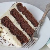 Slice of three layer chocolate cake on a white plate with fork