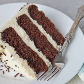 Slice of three layer chocolate cake on a white plate with fork