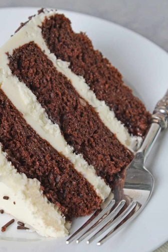 Slice of three layer chocolate cake on a white plate with fork