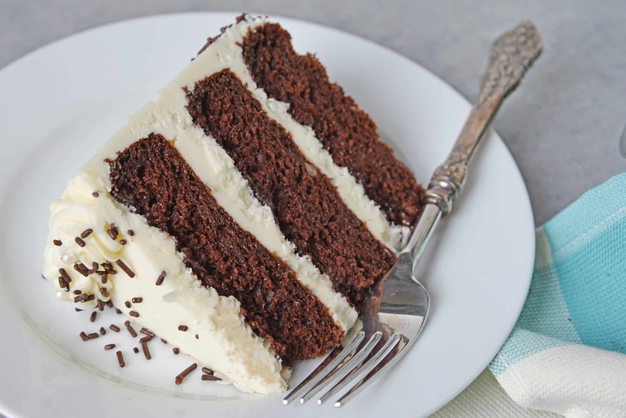 Slice of three layer chocolate cake on a white plate with fork