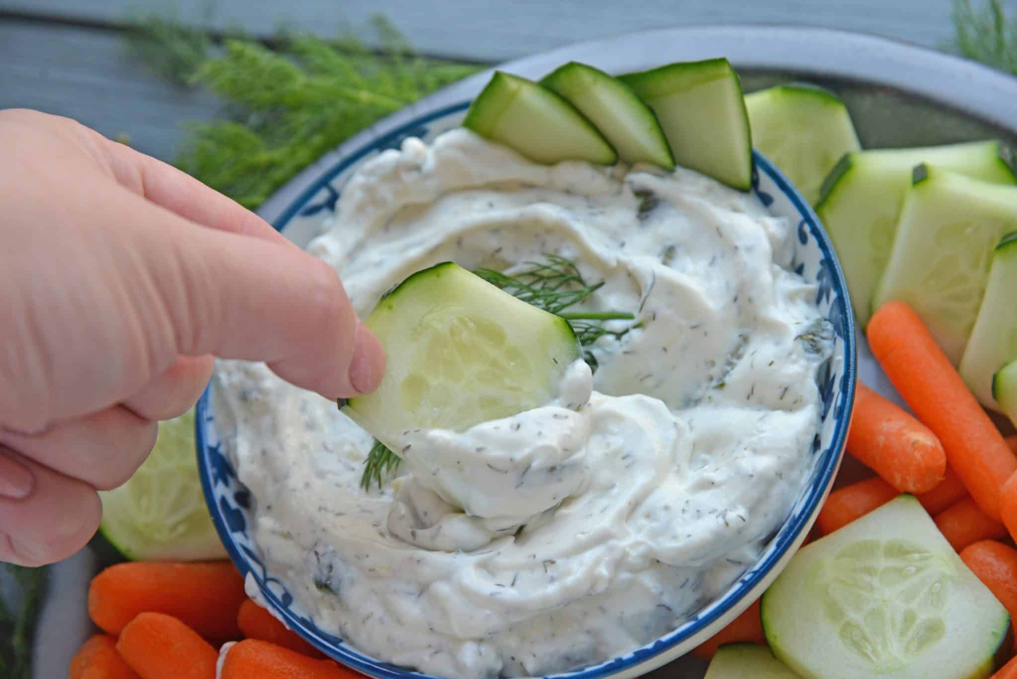hand dipping a cucumber into Garlic Tzatziki Sauce 