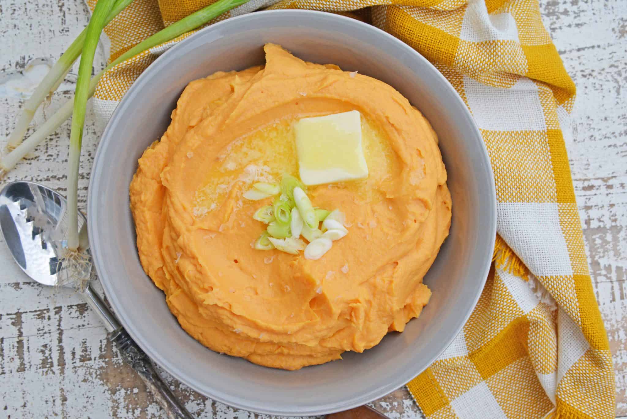 mashed sweet potatoes in a gray bowl with butter and scallions