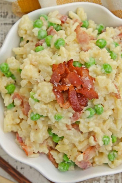 Creamy Parmesan Risotto takes the most traditional risotto recipe and adds vibrant peas and crispy bacon. Sauteed in bacon fat, this rice packs a flavor punch! #parmesanrisottorecipe #easyrisottorecipe www.savoryexperiments.com