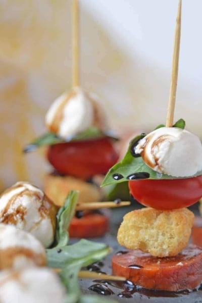 Caprese Skewers are the perfect party appetizer made with fresh mozzarella, basil, tomatoes, garlicky croutons, and zesty pepperoni, all drizzled with a tangy balsamic reduction sauce! #capresesalad #capreseappetizer www.savoryexperiments.com