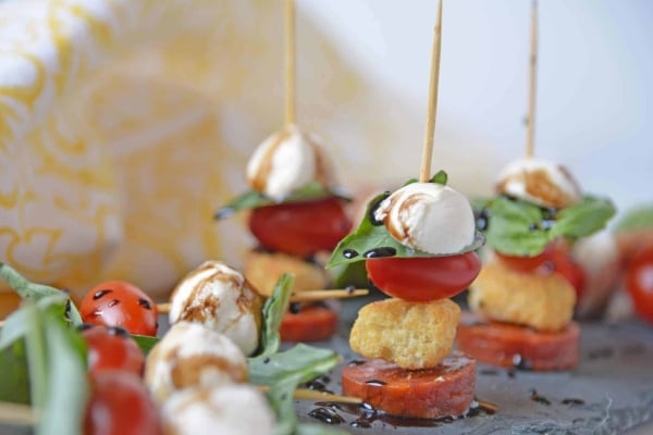 Caprese Skewers are the perfect party appetizer made with fresh mozzarella, basil, tomatoes, garlicky croutons, and zesty pepperoni, all drizzled with a tangy balsamic reduction sauce! #capresesalad #capreseappetizer www.savoryexperiments.com