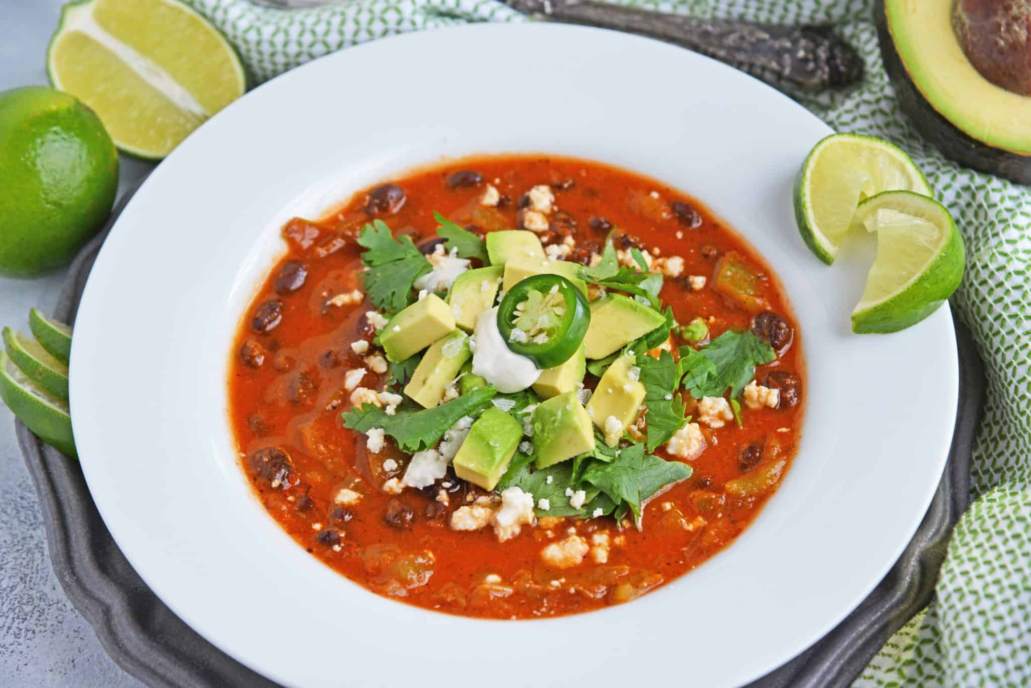 Black bean green chile soup is a tomato based soup with smoky chipotle peppers and robust flavors. Top with avocado, cilantro and queso fresco! #easysoups #souprecipes www.savoryexperiments.com