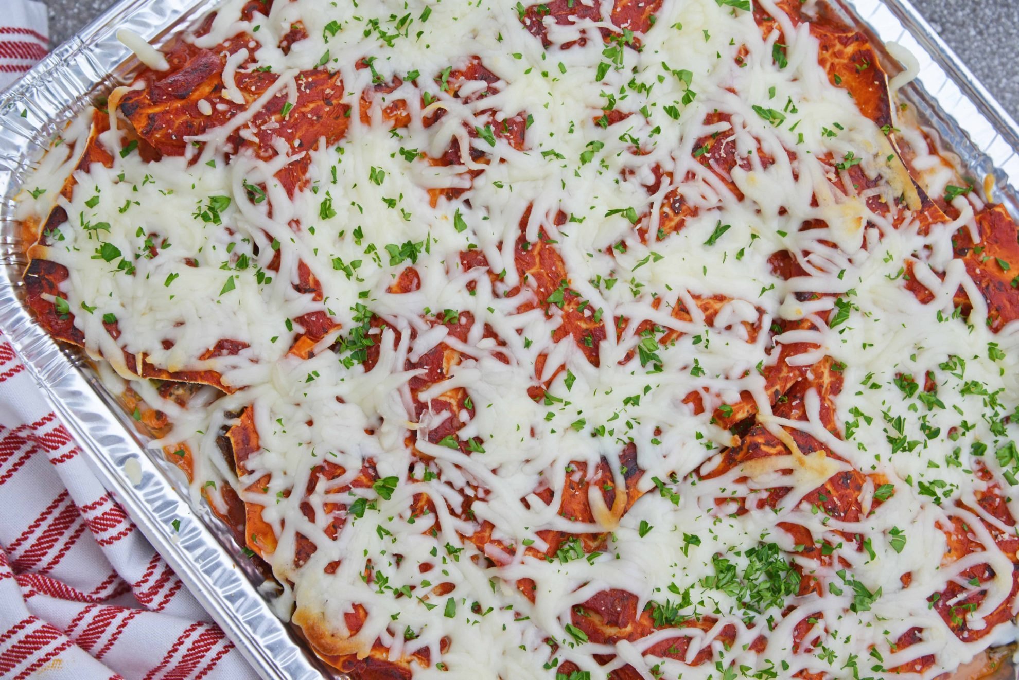 overhead of no boil lasagna in an aluminum pan with grated cheese and parsley 