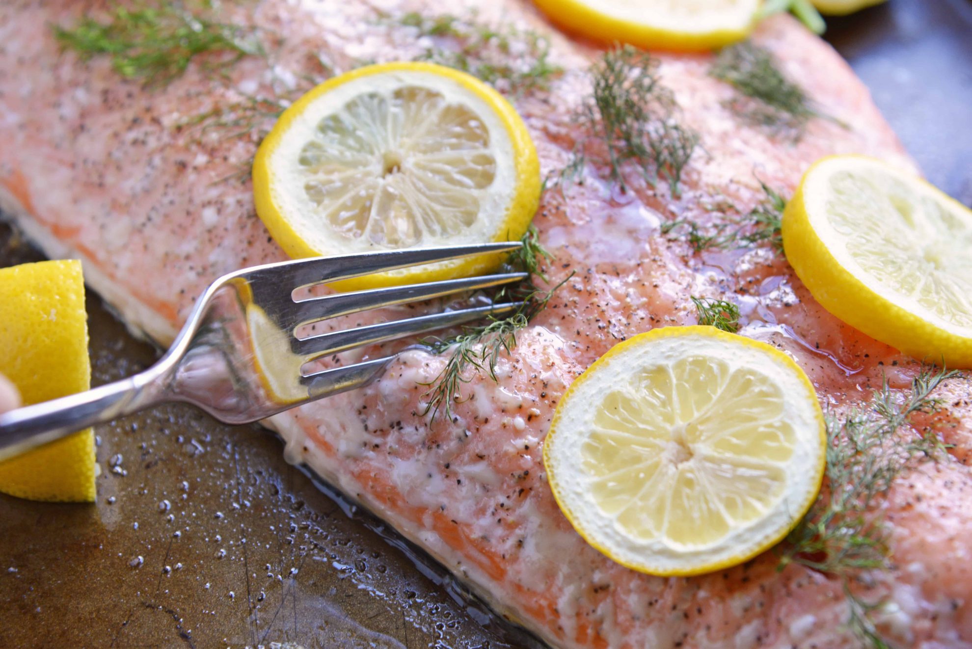 Fork cutting into salmon fillet with lemon slices