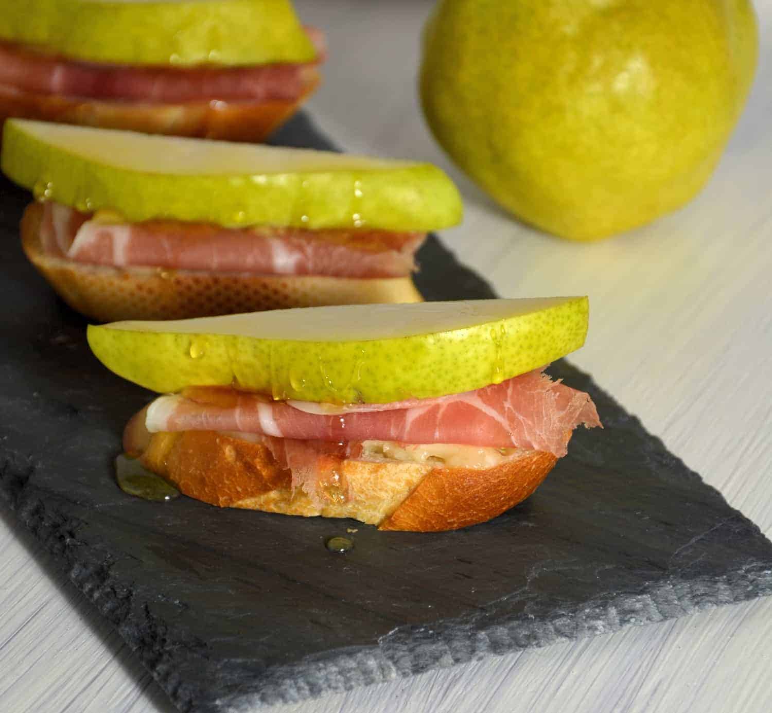 Prosciutto, Pear, and Brie Crostinis fit the bill for any party with tender prosciutto draped over warm brie and topped with a slice of pear and honey. #prosciutto #briecrostinis #crostinis www.savoryexperiments.com