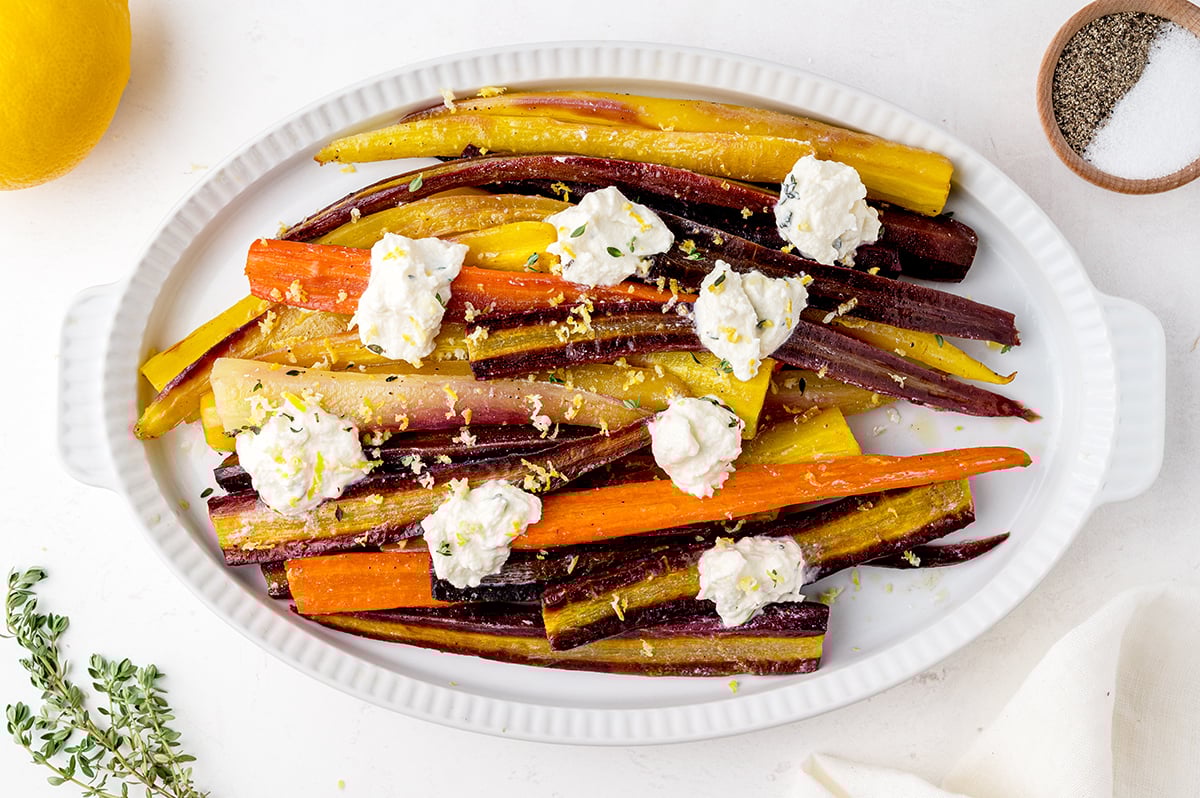 overhead of roasted carrots on a serving platter with ricotta cheese dollops