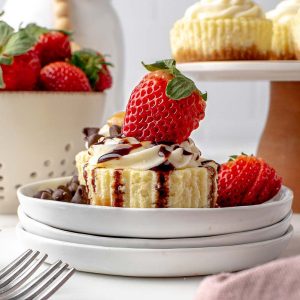 head-on cheesecake cupcakes with cream cheese frosting, chocolate syrup and a fresh strawberry