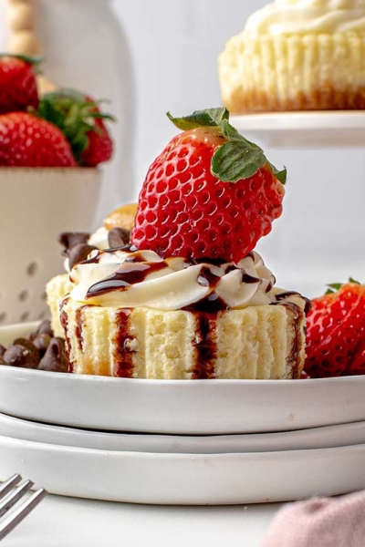 head-on cheesecake cupcakes with cream cheese frosting, chocolate syrup and a fresh strawberry