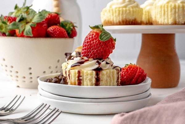 head-on cheesecake cupcakes with cream cheese frosting, chocolate syrup and a fresh strawberry