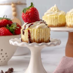 single cheesecake cupcakes on a stand with strawberry and sauce