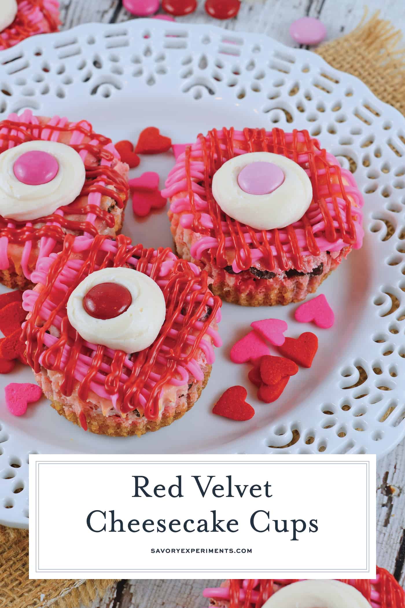Red Velvet Cheesecake Cups are mini bites of creamy cheesecake with a vanilla cookie crust. Topped with a drizzle of chocolate, cream cheese frosting and red velvet M&Ms. #redvelvet #cheesecakecups www.savoryexperiments.com
