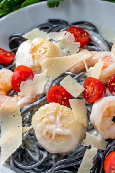 Overhead shot of black pasta in a white bowl with shrimp and scallops