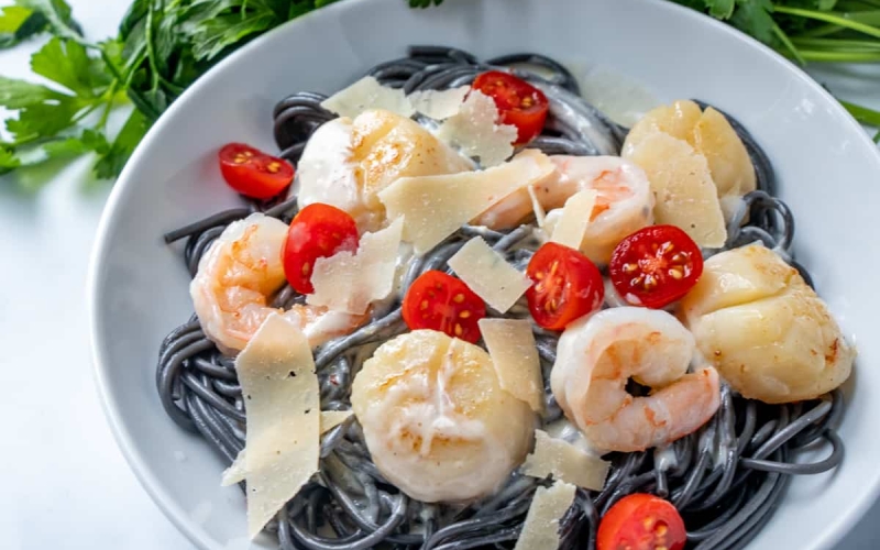 Overhead shot of black pasta in a white bowl with shrimp and scallops