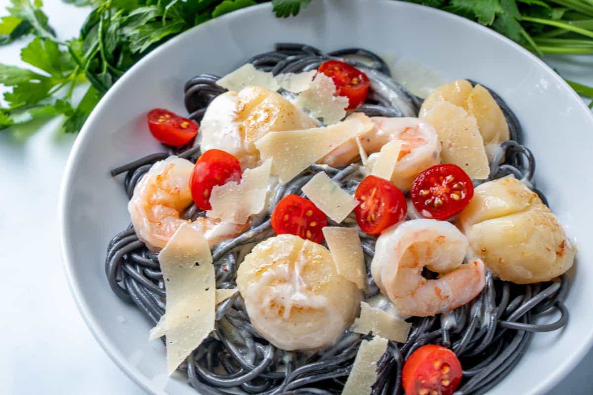 Overhead shot of black pasta in a white bowl with shrimp and scallops