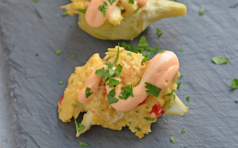 Crab Dip Stuffed Artichoke Hearts takes traditional hot crab dip and bakes in an artichoke heart, topping it with crunchy panko and Sriracha Aioli. #hotcrabdip #artichokerecipes #crabappetizers www.savoryexperiments.com