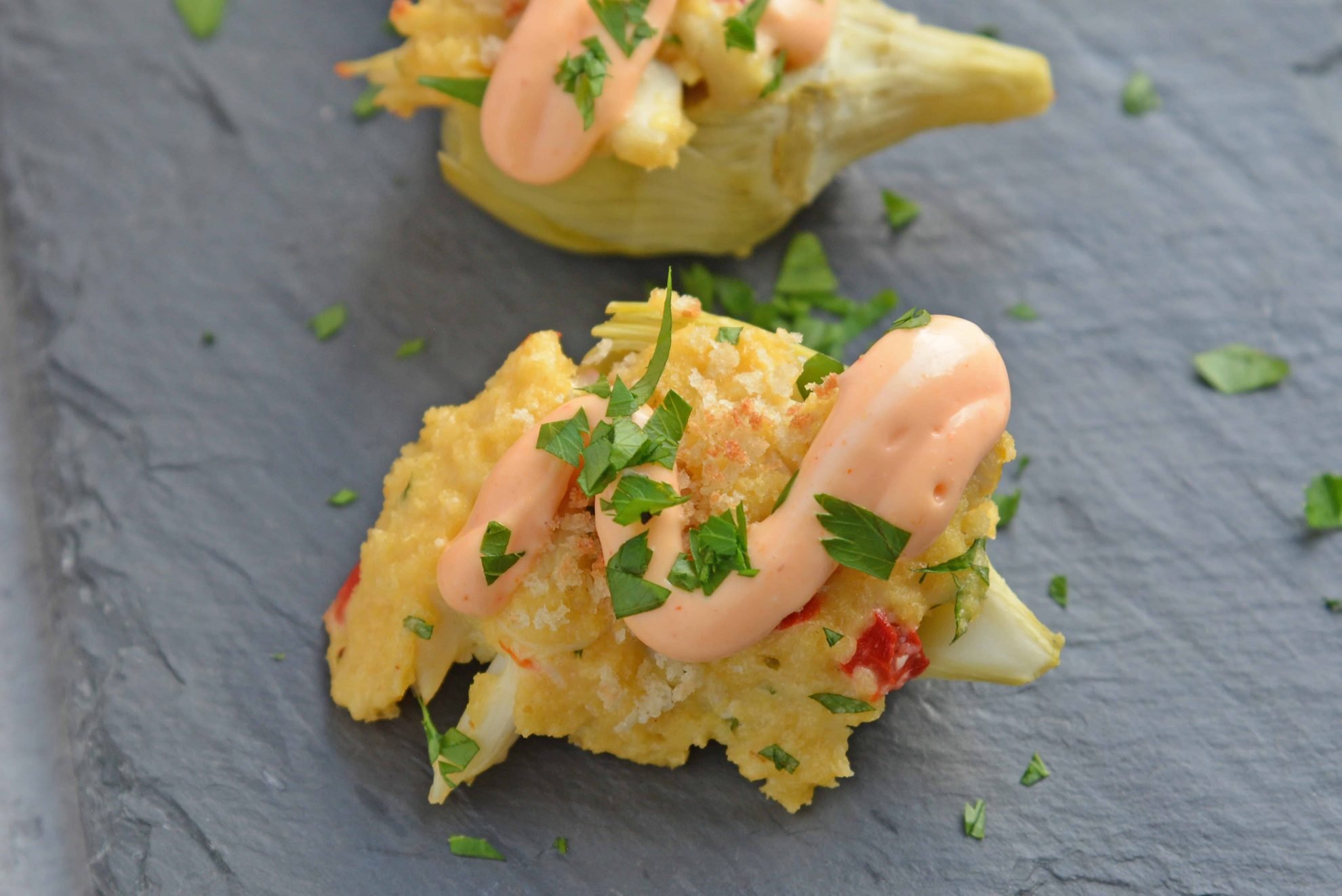 Crab Dip Stuffed Artichoke Hearts takes traditional hot crab dip and bakes in an artichoke heart, topping it with crunchy panko and Sriracha Aioli. #hotcrabdip #artichokerecipes #crabappetizers www.savoryexperiments.com