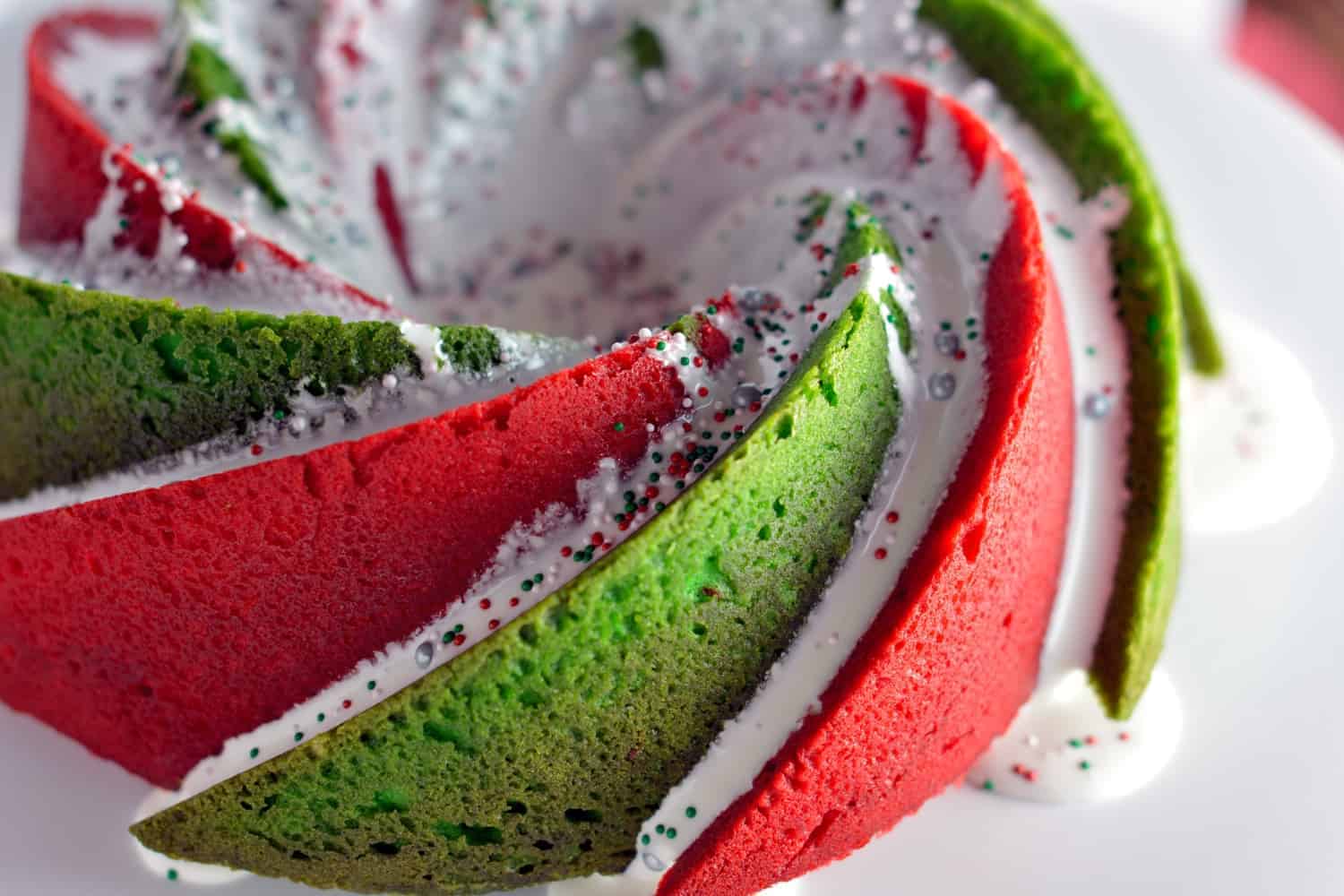 Christmas Bundt Cake is a delicious vanilla pound cake tinted with red and green swirls with a marshmallow fluff icing. Make this show stopping cake today! #bundtcakerecipes #christmascakes www.savoryexperiments.com 