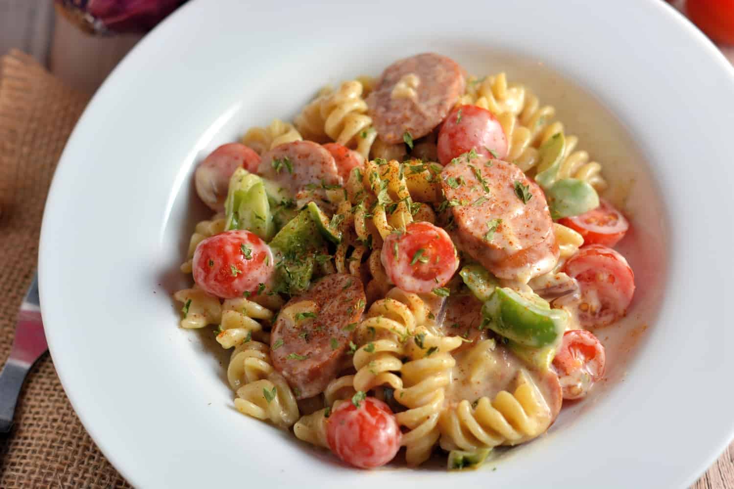 Creamy Cajun Pasta is rotini in a cream sauce with cajun seasoning, smoky andouille sausage, sautéed peppers, red onion and grape tomatoes. Takes 20 minutes to make! #cajunpasta #easypastadishes www.savoryexperiments.com 