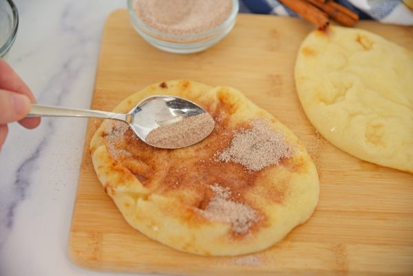 spooning cinnamon sugar onto flatbread