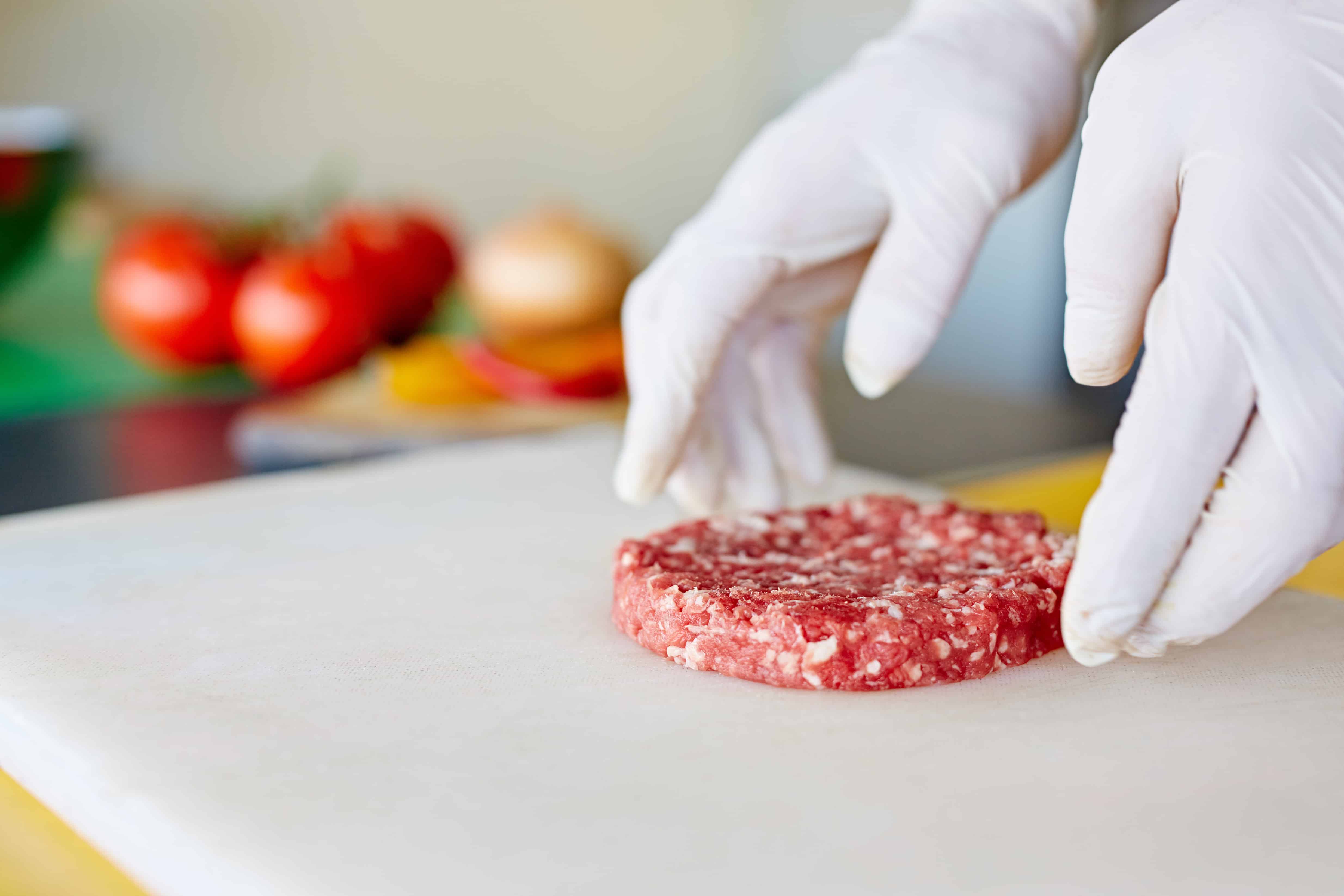 gloved hands showing how to make a burger patty using ground beef 