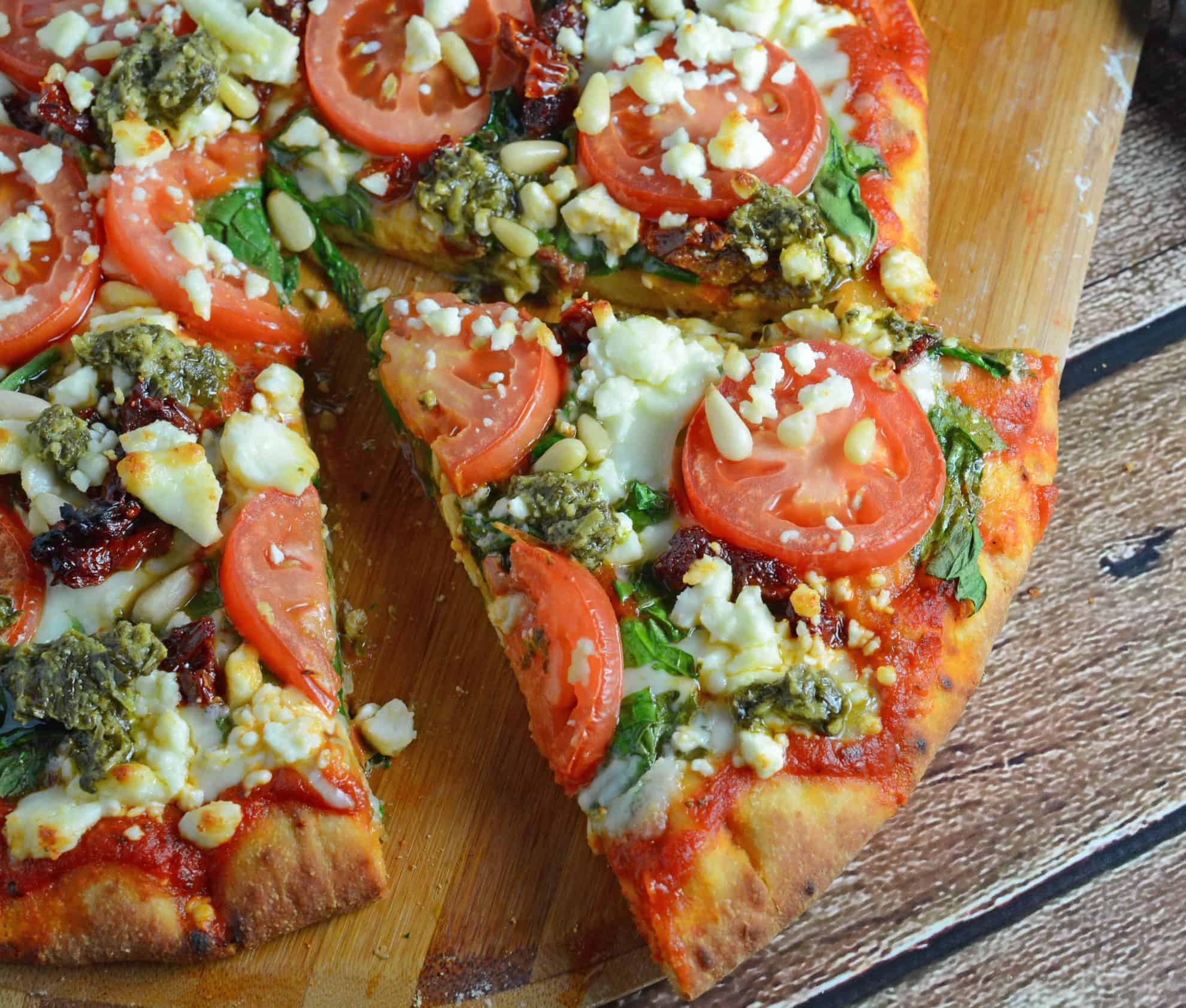 Tomato Pesto Pizza is an easy vegetarian pizza with fresh tomato slices, mozzarella and feta cheese, sun dried tomatoes, pesto and toasted pine nuts. #homemadepizza #pizzafromscratch #pestopizza www.savoryexperiments.com 