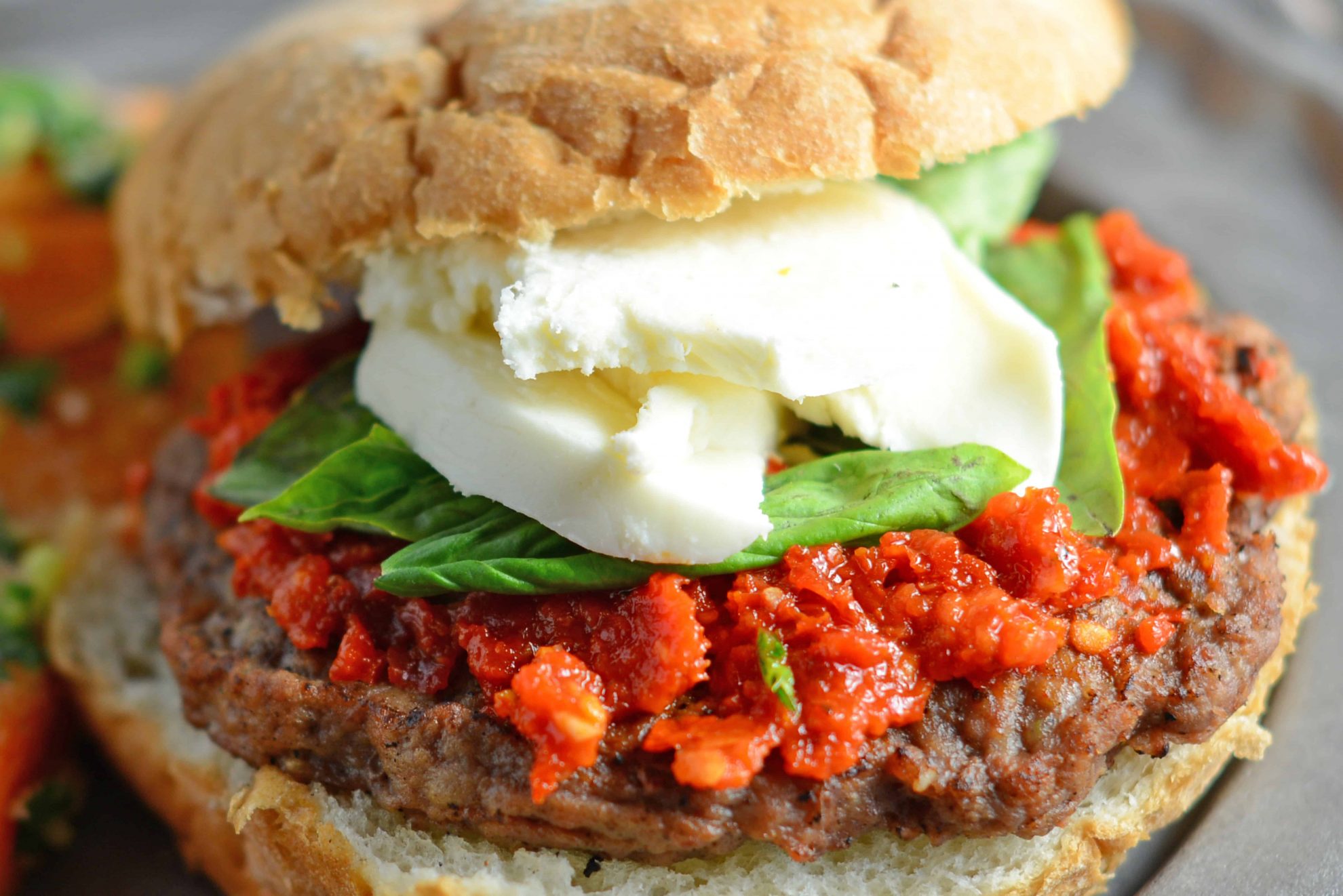 Caprese Burgers are smothered with a red pesto, fresh mozzarella and basil all on a flame-grilled burger. The best gourmet burger out there! #capreseburgers #gourmetburgers www.savoryexperiments.com