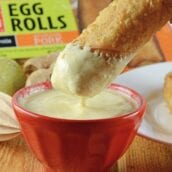 egg roll dipping into a coconut curry sauce in a red bowl