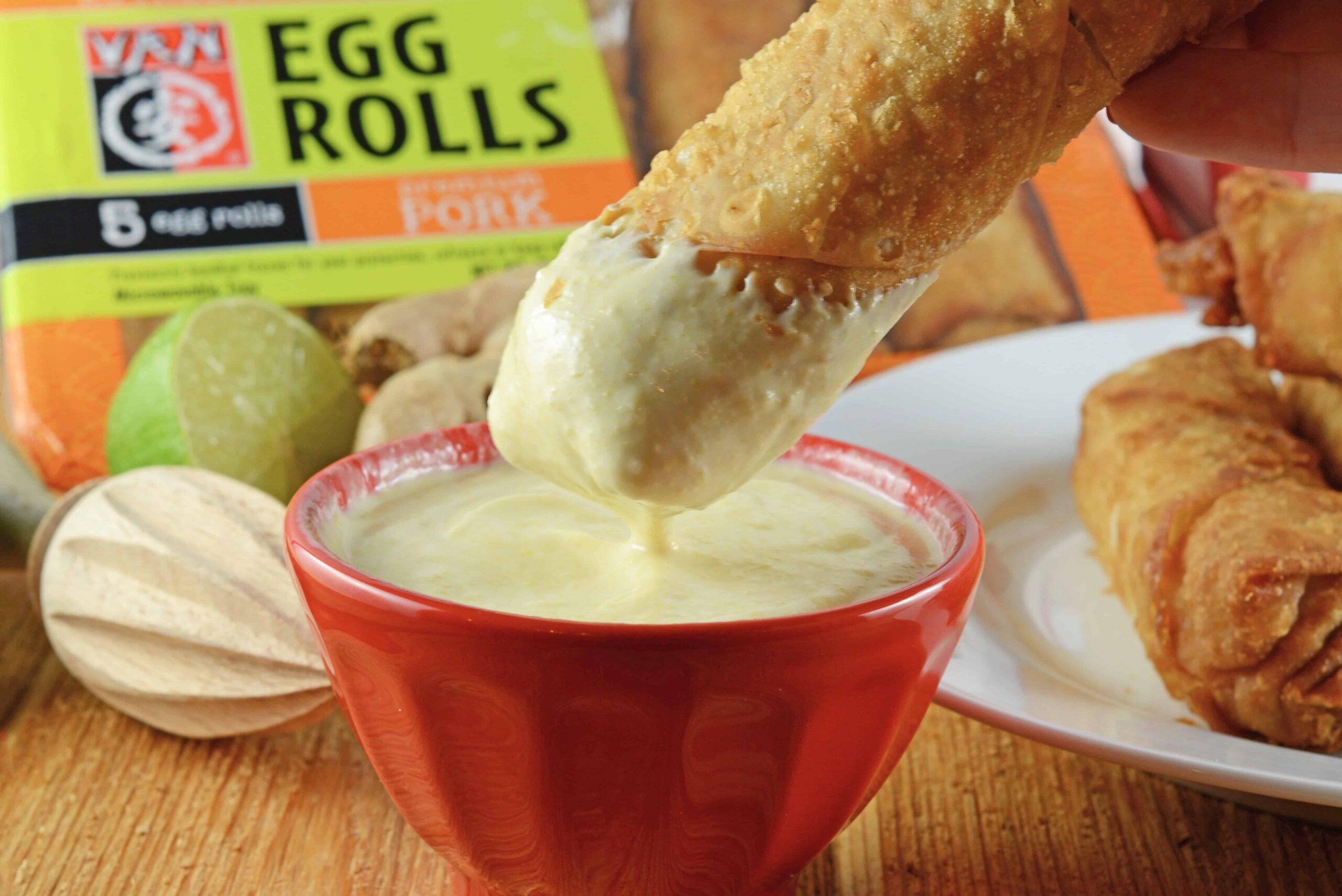 egg roll dipping into a coconut curry sauce in a red bowl