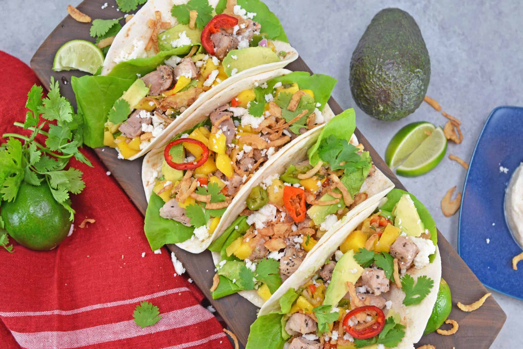 Crispy Pork Tacos are soft tacos filled with mango salsa, cool avocado, crumbly queso fresco, butter lettuce and crispy onion straws. 