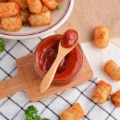 spicy ketchup in a glass bowl with a wooden spoon and tater tots