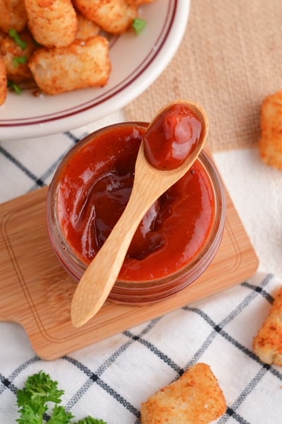 spicy ketchup in a glass bowl with a wooden spoon and tater tots