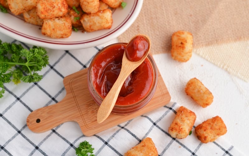 spicy ketchup in a glass bowl with a wooden spoon and tater tots