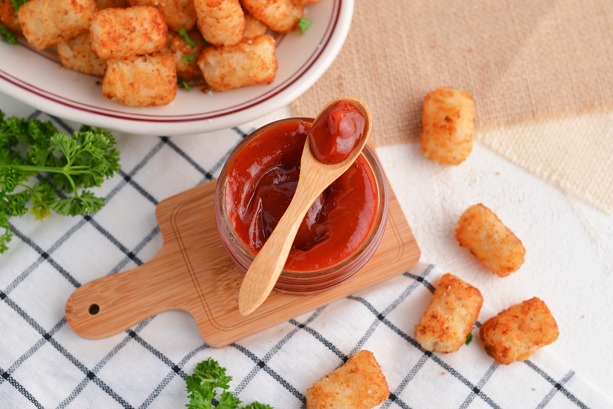 spicy ketchup in a glass bowl with a wooden spoon and tater tots