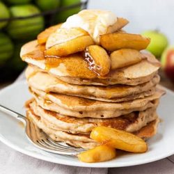 Apple pie pancakes on a white plate topped with apples