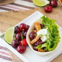 Cherry chicken taco boat on a white plate with fresh cherries