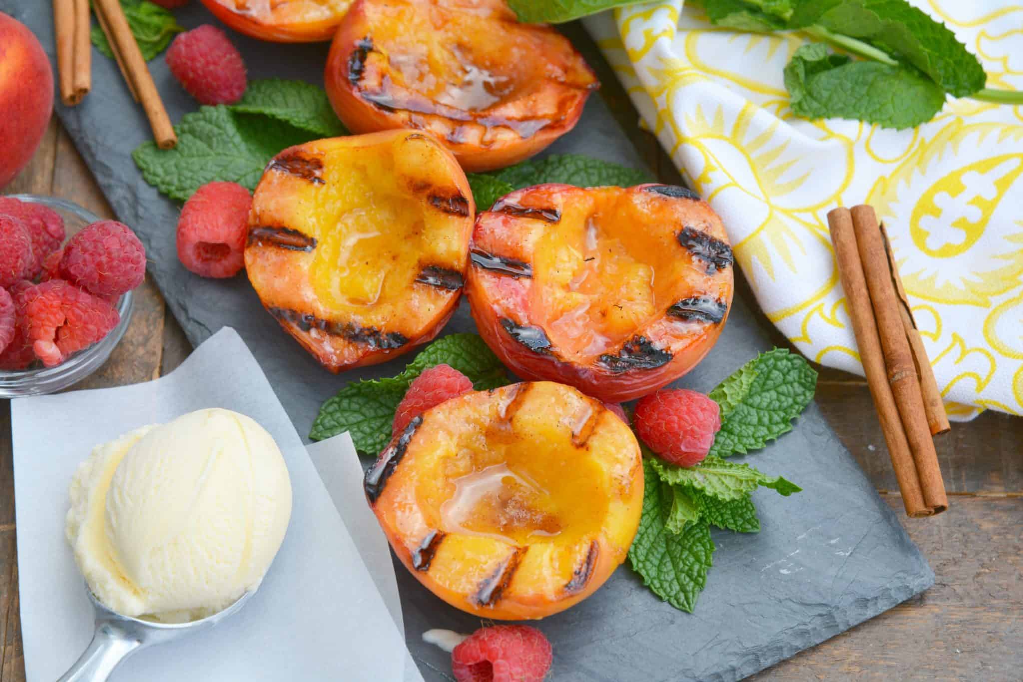 Grilled Peaches basted with cinnamon brown sugar and butter are the ultimate summer dessert idea. Add vanilla ice cream and fresh raspberries for dessert perfection! #grilledpeaches www.savoryexperiments.com