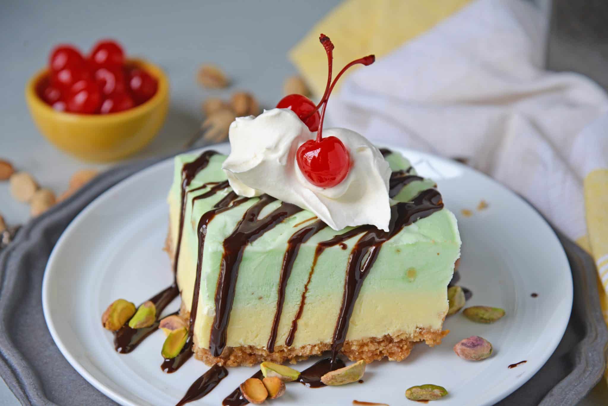 This no-bake cake is layered with graham crackers, vanilla and pistachio pudding and topped with chopped pistachios, chocolate sauce and cherries! #iceboxcake #pistachioiceboxcake #pistachiocake www.savoryexperiments.com