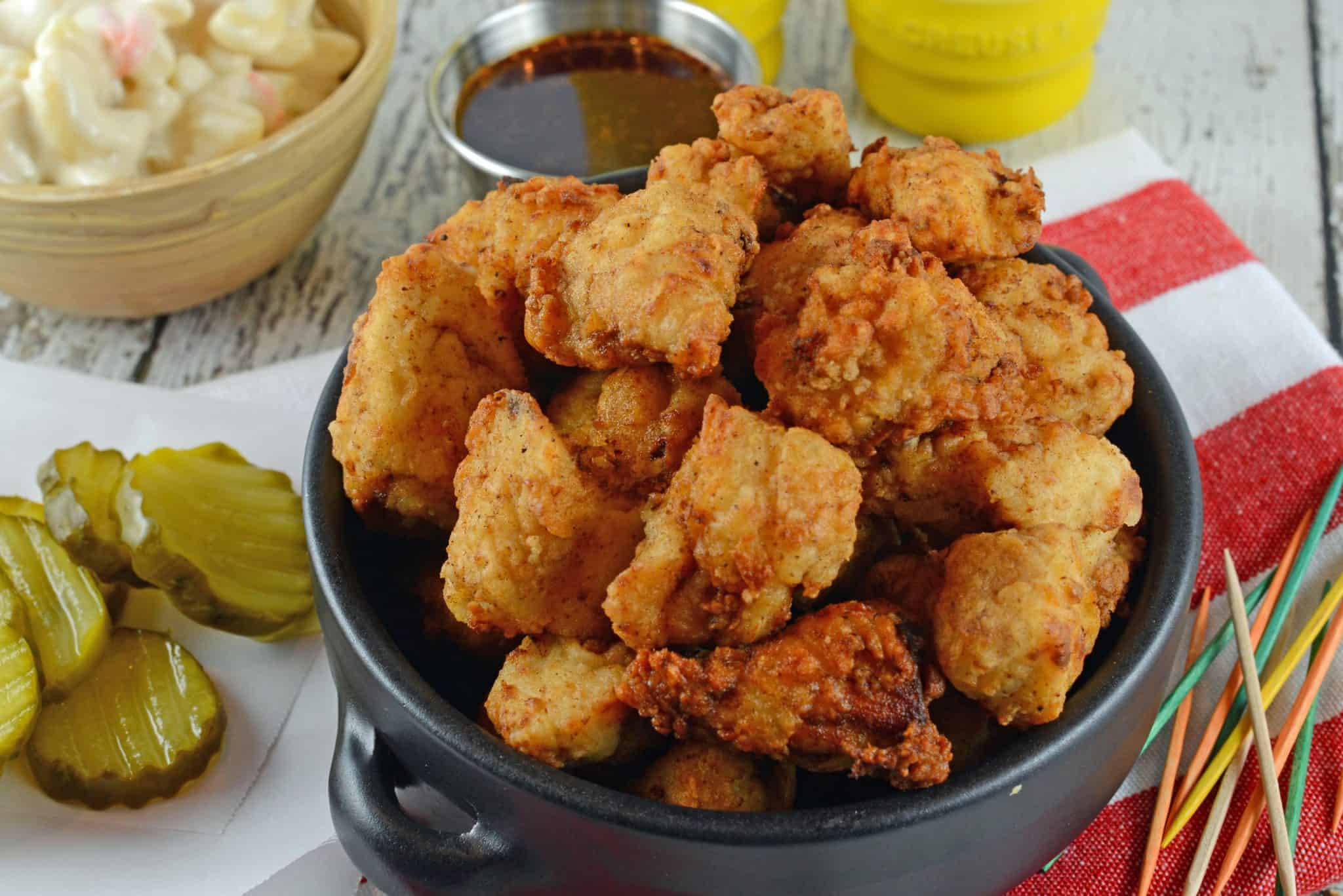 Popcorn chicken in a black bowl with pickles. 