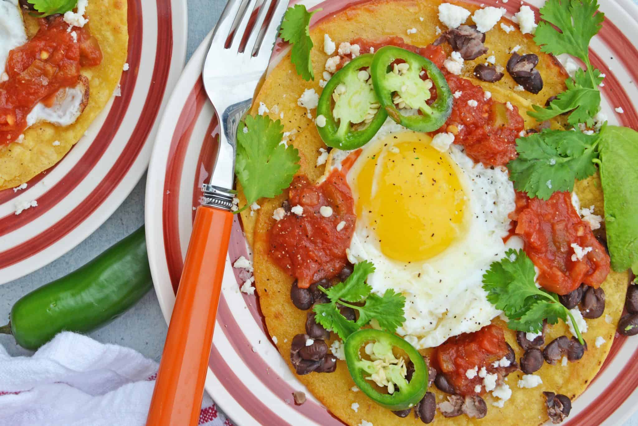 Huevos Rancheros are a great way to spice up your breakfast. Lacey eggs with a runny yolk over warm corn tortillas, chunky salsa, black beans, cilantro and queso fresco. #huevosrancheros www.savoryexperiments.com