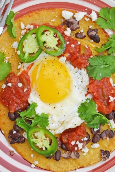 Huevos Rancheros are a great way to spice up your breakfast. Lacey eggs with a runny yolk over warm corn tortillas, chunky salsa, black beans, cilantro and queso fresco. #huevosrancheros www.savoryexperiments.com