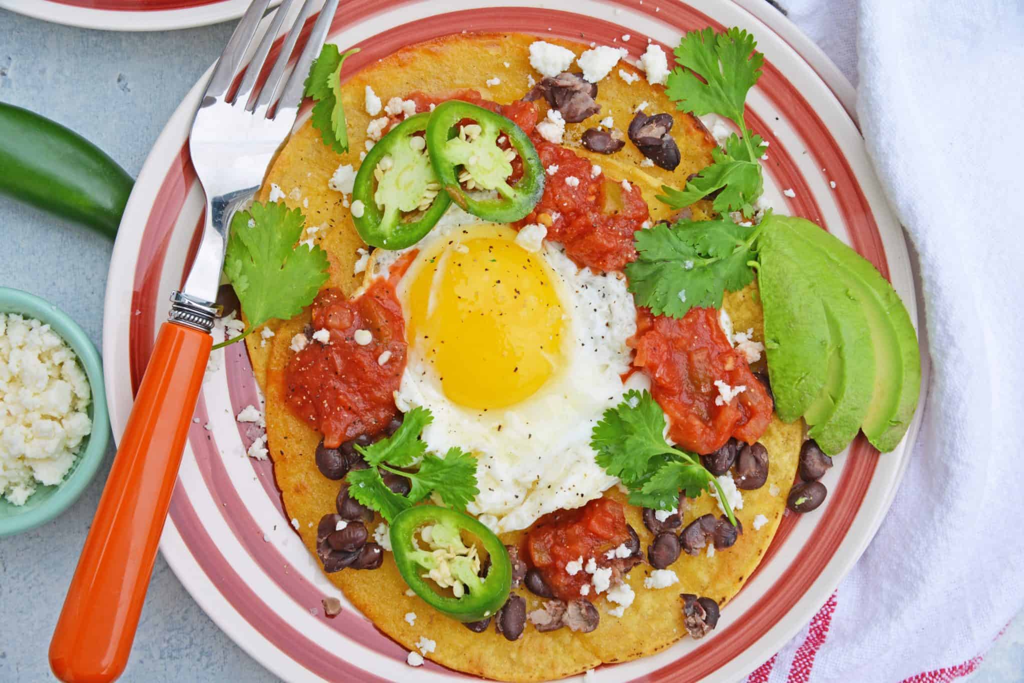 Huevos Rancheros are a great way to spice up your breakfast. Lacey eggs with a runny yolk over warm corn tortillas, chunky salsa, black beans, cilantro and queso fresco. #huevosrancheros www.savoryexperiments.com